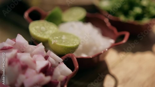 Clay pots of chopped radishes, onions, lettuce, and limes on wooden table
