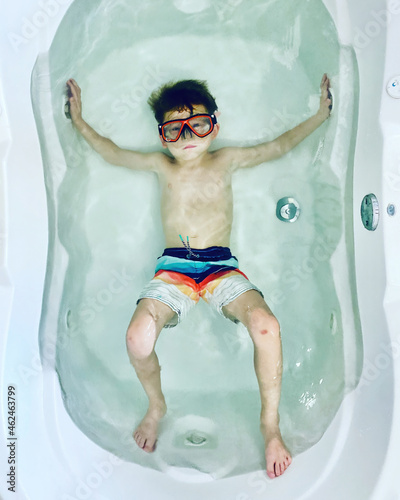 Moody boy in a large bathtub wearing swim trunks and a diving mask photo