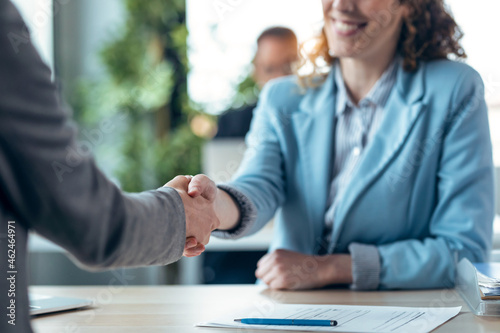 Attractive real-estate agent shaking hands with woman after signing agreement contract in a real estate
