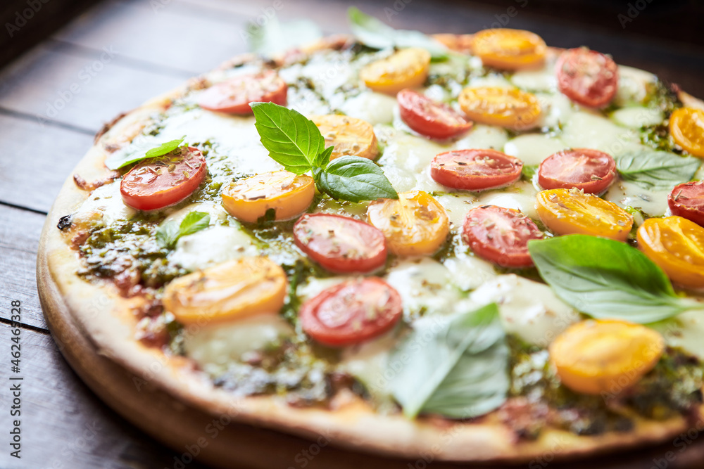 Pizza with cherry tomatoes, mozzarella and basil pesto. Dark wooden background. Close up. 