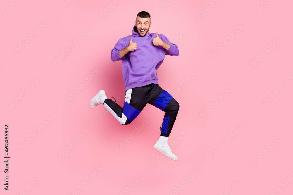 Full length photo of young cheerful man jump show thumbs-up select suggest advertise isolated over pink color background Full length photo of young cheerful man jump show thumbs-up select suggest advertise isolated over pink color background