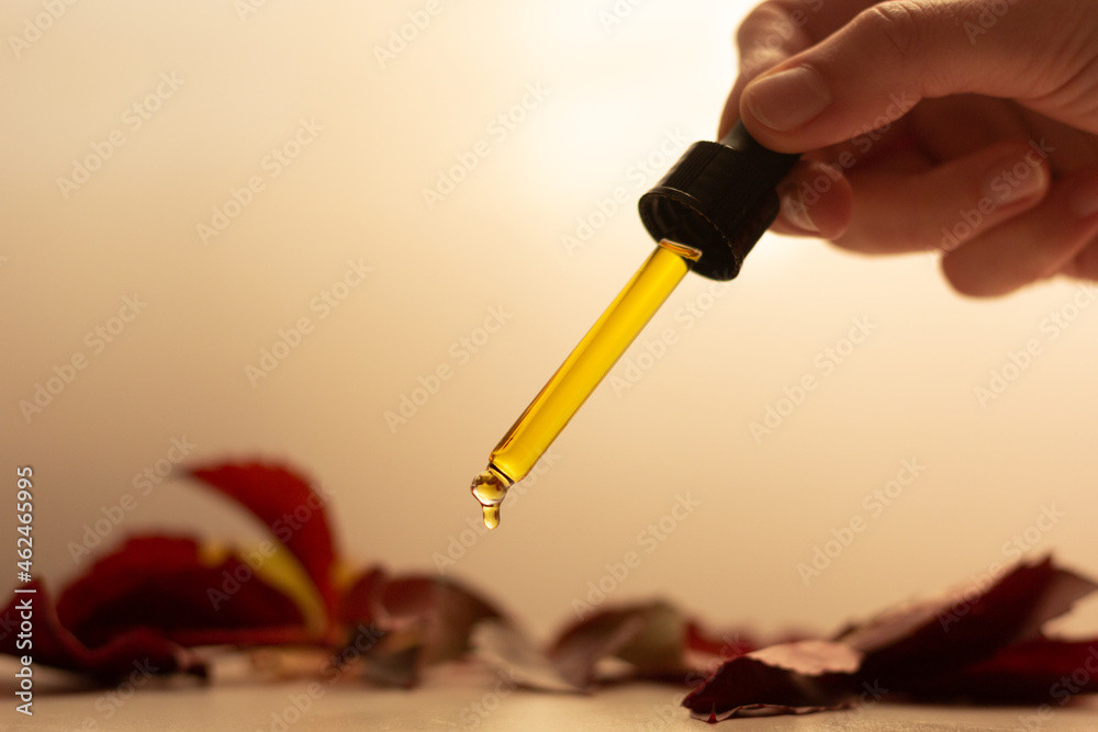 Concept of autumn skincare. Closeup of a pipette of serum and dry leaves.