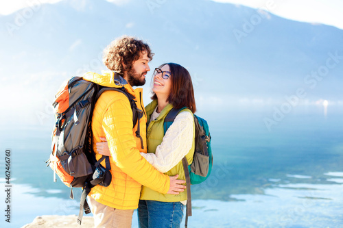 Travelers with hiking backpacks by mountains, autumn sea. Happy young couple