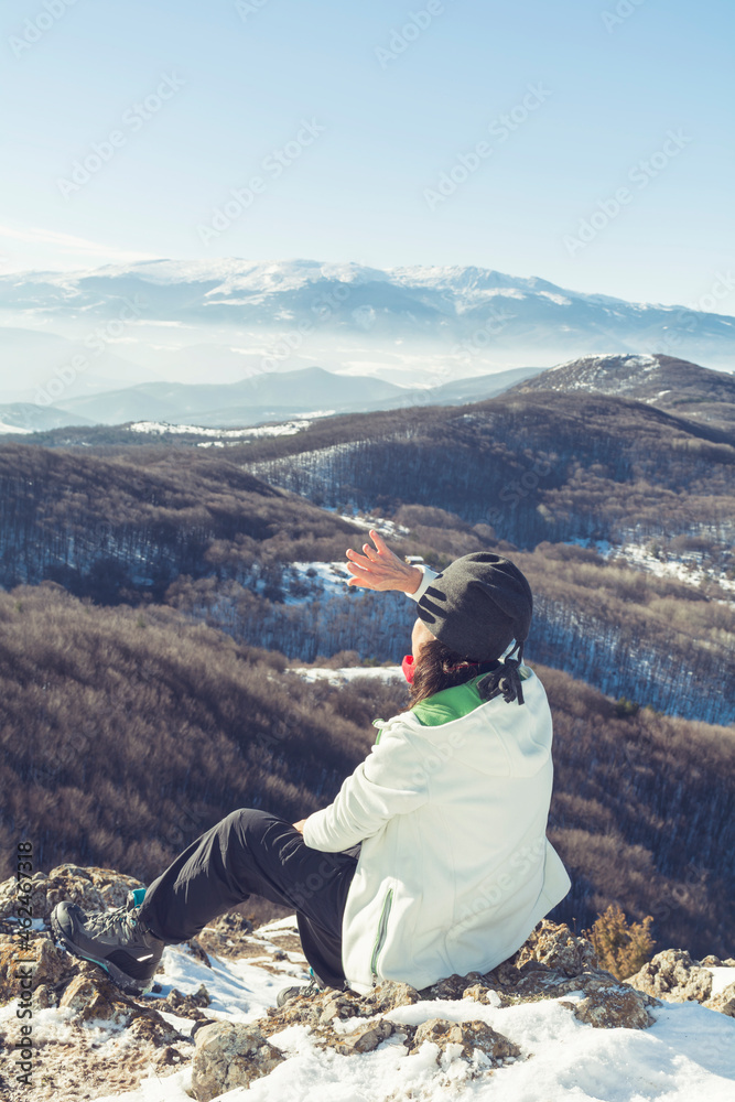 Back view of  woman with hat sitting and enjoying the high mountain view in the winter . Polovrak peak in Bulgaria 