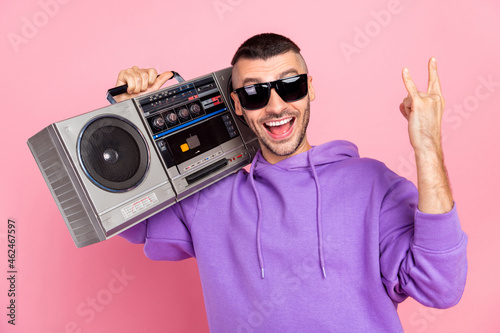 Photo of funny young brunet guy hold boom box show rock sign wear eyewear hoodie isolated on pink background