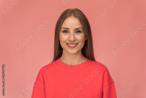 Waist up portrait view of a beautiful happy young woman standing on a pink wall and sincerely smiling. Modern girl smiling broadly at camera, while standing against pink background