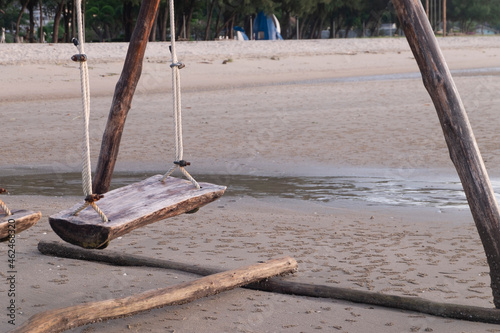 The wooden swing sits on the sand by the sea.