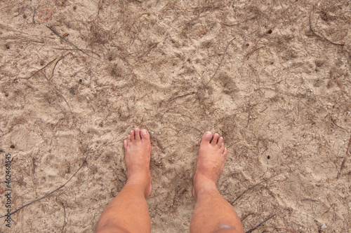 Two feet of an Asian man standing on the sandy shore.