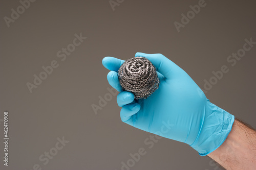 New kitchen metal wire scrubber held in hand by Caucasian male hand wearing a blue latex glove. Close up studio shot, isolated on gray background photo