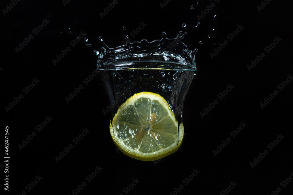 Lemon slices fall into water on a black background. Fresh lemon drink