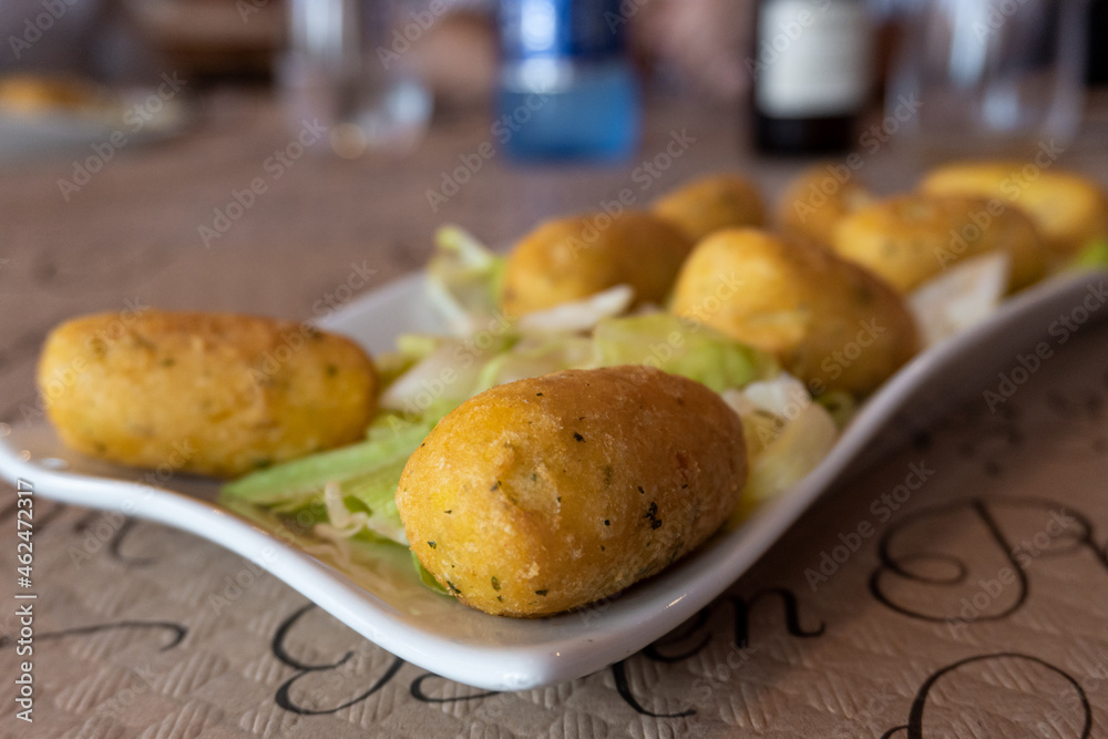 Macro closeup with selective focus on some cod croquettes, on a lettuce background, on a white plate.