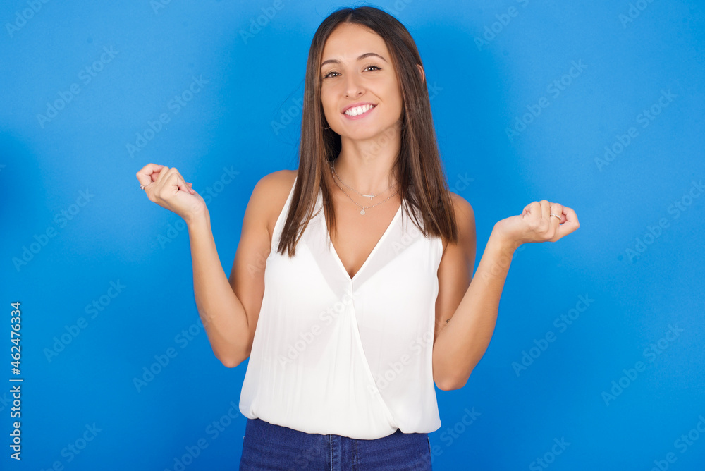 Young european brunette woman wearing white T-shirt on blue background, making money gesture. Young european brunette woman wearing white T-shirt on blue background, making money gesture.