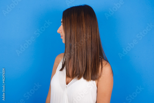 Side view of young happy smiling Young european brunette woman wearing white T-shirt on blue background