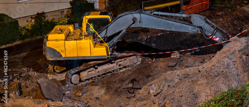 Construction site on a city street. A yellow digger excavator parked during the night on a construction site