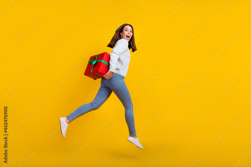 Full size photo of happy young woman jump hold gift spine hide amazed isolated on yellow color background