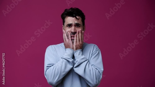 the guy did something bad and he is very uncomfortable because of this, he is dressed in a light blue blouse, the background is pink