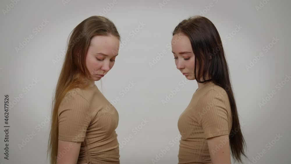 Identical twin sisters with red and black hair imitating touching glass standing at grey background. Slim beautiful Caucasian women imitating mirror. Sisterhood concept Identical twin sisters with red and black hair imitating touching glass standing at grey background. Slim beautiful Caucasian women imitating mirror. Sisterhood concept