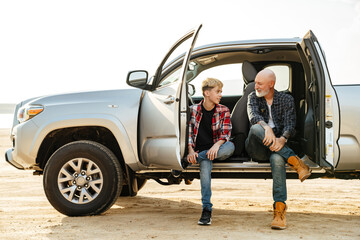 Smiling father and his son sitting in a car trunk