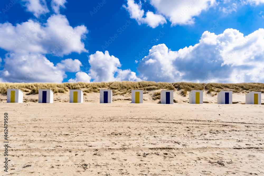 Little beach cabins at a North Sea. White little houses on the deserted  sand dunes of Netherlands  with blue cloudy sky.