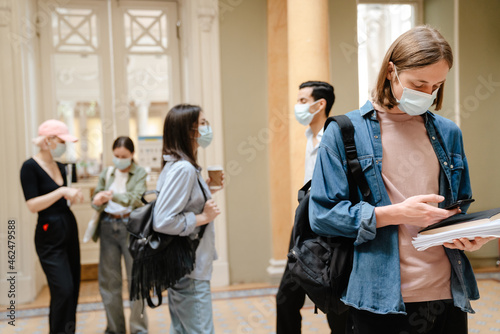 Young european students in face mask standing at library hallway