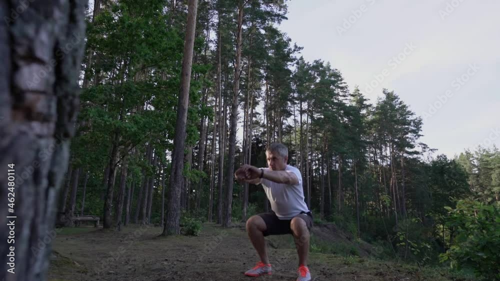 Caucasian mature person doing squat exercise with bodyweight in forest. Sporty and wellness lifestyle concept. Caucasian mature person doing squat exercise with bodyweight in forest. Sporty and wellness lifestyle concept.