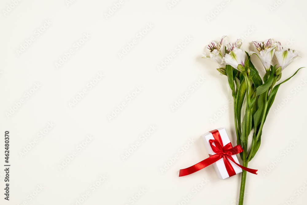 alstroemeria flowers and a gift box with a red satin ribbon on the beige background. happy birthday greetings. with love. happy celebration. a greeting card. top view, flat lay alstroemeria flowers and a gift box with a red satin ribbon on the beige background. happy birthday greetings. with love. happy celebration. a greeting card. top view, flat lay