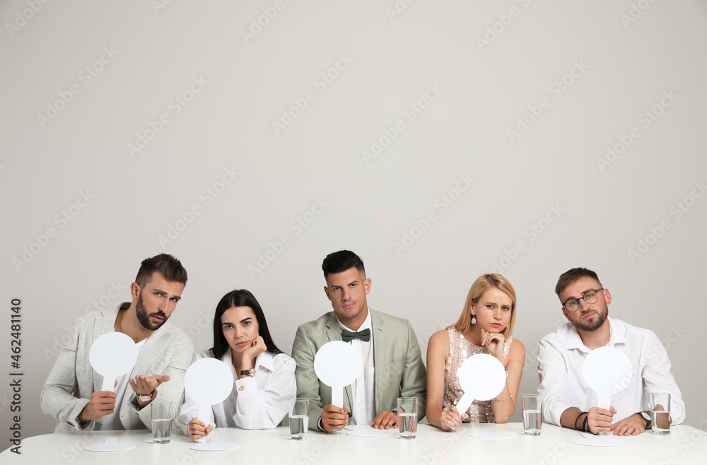 Panel of disappointed judges holding blank score signs at table on beige background. Space for text Panel of disappointed judges holding blank score signs at table on beige background. Space for text