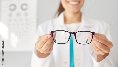 Smiling optician gives you new glasses. Happy doctor in white coat showing modern good quality eyewear. Optometry, prescription for glasses, eye health concept. Banner background, closeup, close up