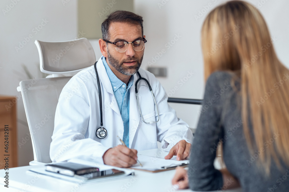 Shot of handsome mature male doctor talking while explaining medical treatment to patient in the consultation. Shot of handsome mature male doctor talking while explaining medical treatment to patient in the consultation.