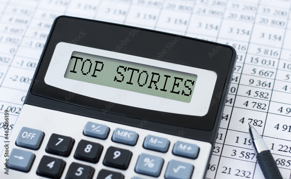 Word TOP STORIES written on the calculator screen against the background of figures, financial statements Word TOP STORIES written on the calculator screen against the background of figures, financial statements