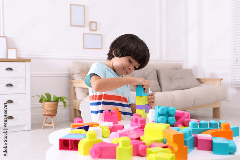 Cute little boy playing with colorful building blocks at table in living room Cute little boy playing with colorful building blocks at table in living room