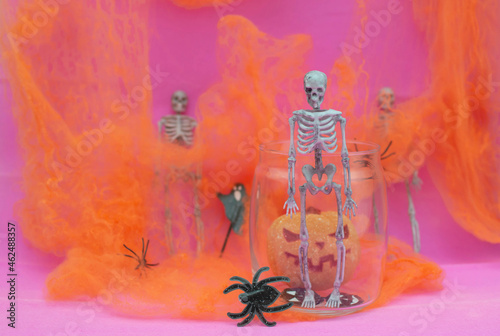 Fototapeta Naklejka Na Ścianę i Meble -  Orange pumpkin, skeletons, black spiders in a web on a pink background. Interior decoration for the Halloween holiday. A place to copy. Selective focus