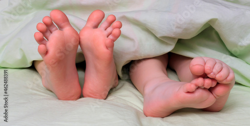 Legs, heels, toes and feet of children lying in bed under a blanket. Close-up of feet of two children, brothers or sisters