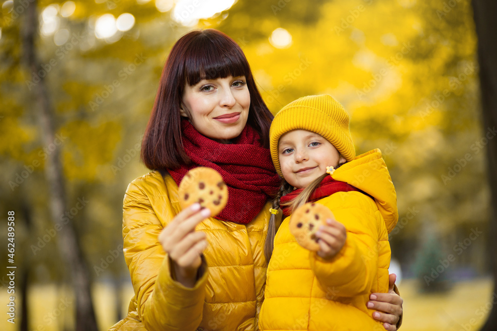 Portrait of beautiful family, mother and little daughter, posing together on fresh air in autumn park with tasty homemade cookies in hands. Selective focus on smiling faces Portrait of beautiful family, mother and little daughter, posing together on fresh air in autumn park with tasty homemade cookies in hands. Selective focus on smiling faces