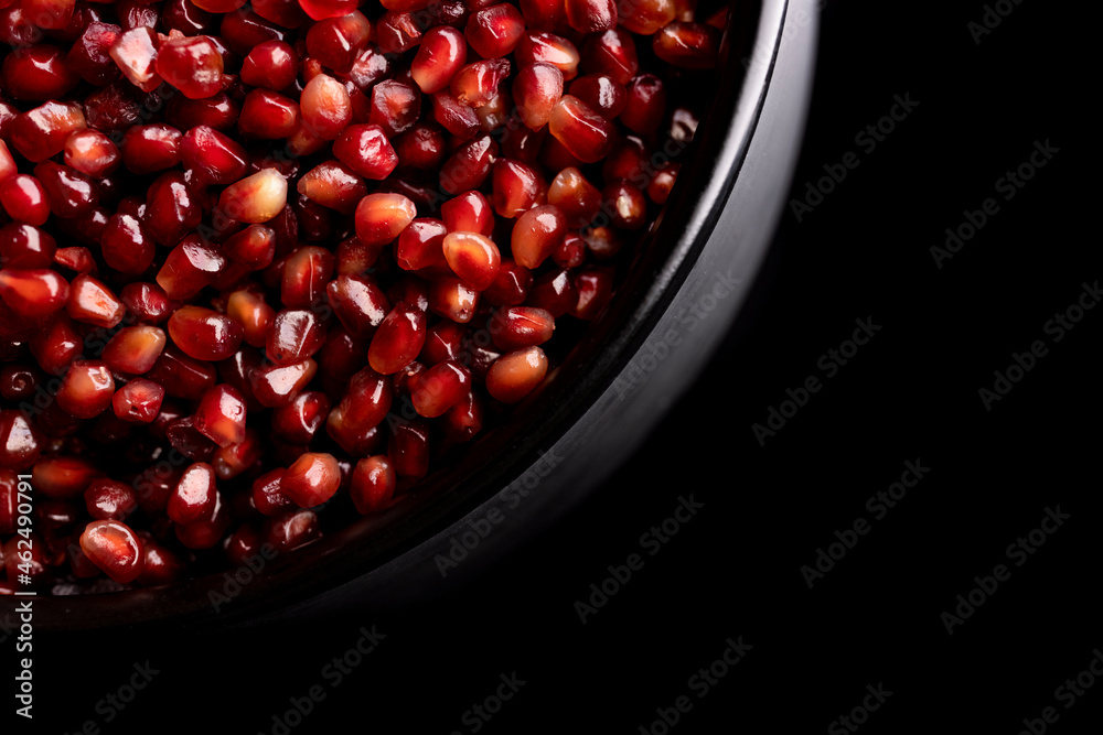 A lot of beautiful red pomegranate seeds in a black bowl A lot of beautiful red pomegranate seeds in a black bowl