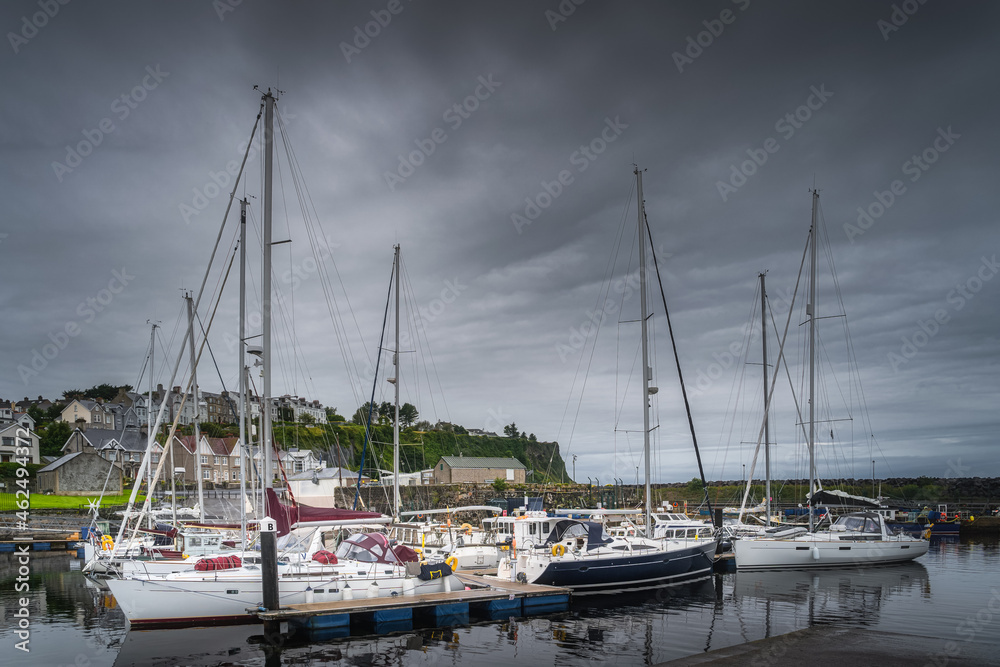 Yachts and sailboats moored in small, beautiful marina in Ballycastle town with birds flying over, Antrim, Northern Ireland