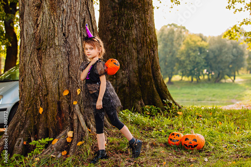 Portrait blonde girl in witch costume with pumpkin in her hands. Halloween kids.