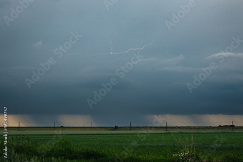 Fallstreaks of rain or hail below the base of thunderstorm. Lightning bolt is weakly visible between the clouds.