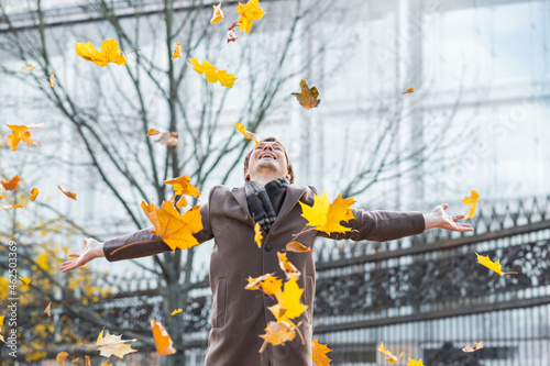 Obraz na płótnie A happy and successful businessman in a brown coat throws yellow maple autumn le