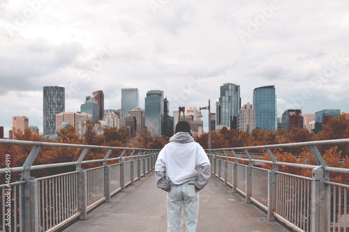 Young teenage girl from behind standing on bridge looking at city in front of her, Bow River Pathway