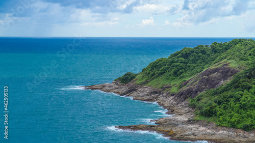 adorable beautiful seascape view show clean and clear aquatic green water with some white wave, rock coast with cliff and forest tree mountain, a sunny daylight cloud in blue sky