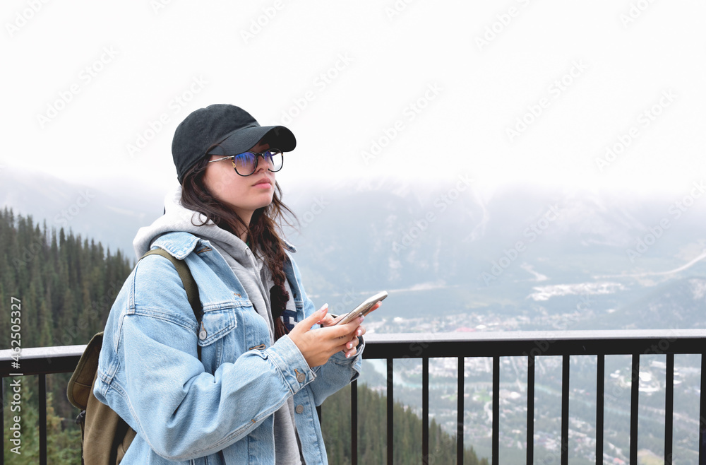 Young girl standing at railing on top of mountain with mobile phone