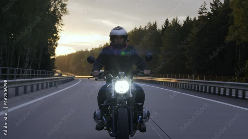 Man riding scrambler motorbike on the highway through the forest at the sunset. Man riding cafe racer on the highway, front view. High quality 4k footage Man riding scrambler motorbike on the highway through the forest at the sunset. Man riding cafe racer on the highway, front view. High quality 4k footage