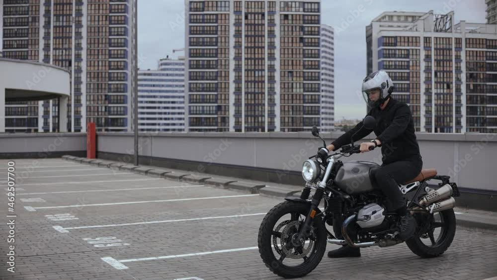 Young man starts scrambler motorbike on top of the multi-level parking in city. Guy riding cafe racer in empty parking garage. High quality 4k footage Young man starts scrambler motorbike on top of the multi-level parking in city. Guy riding cafe racer in empty parking garage. High quality 4k footage