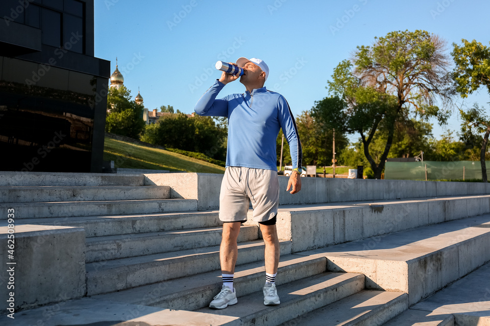 Sporty mature man drinking water on stairs outdoors Sporty mature man drinking water on stairs outdoors
