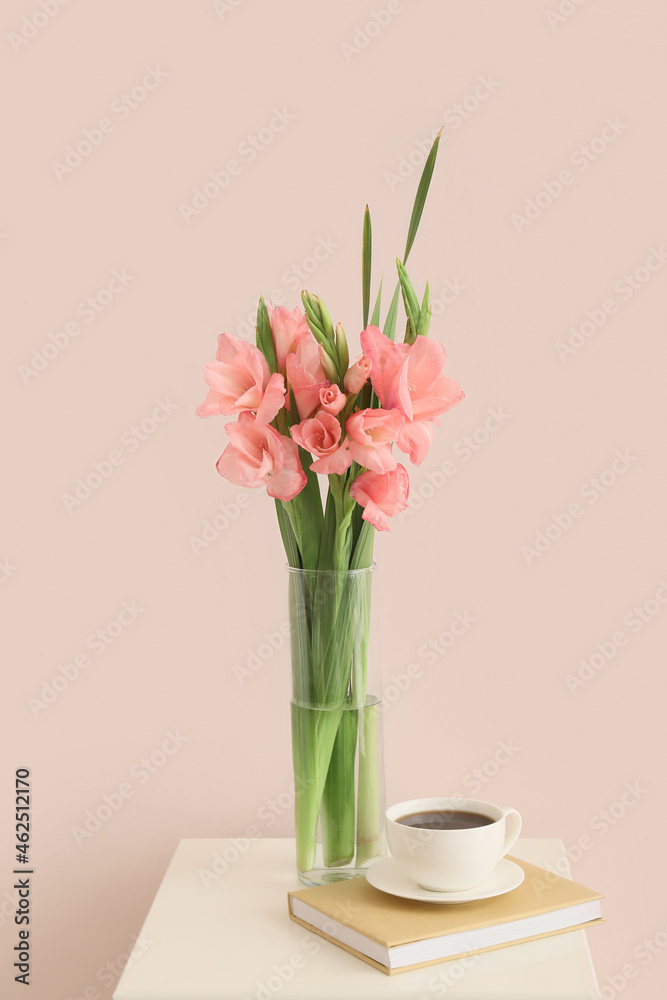 Vase with gladiolus flowers, cup of coffee and book on table in room