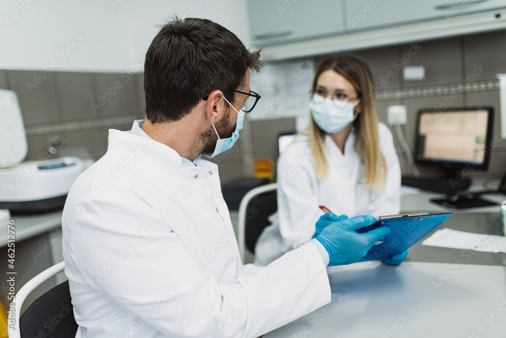 Fototapeta premium Two scientists or technicians with face protective masks work in laboratory on human blood samples.
