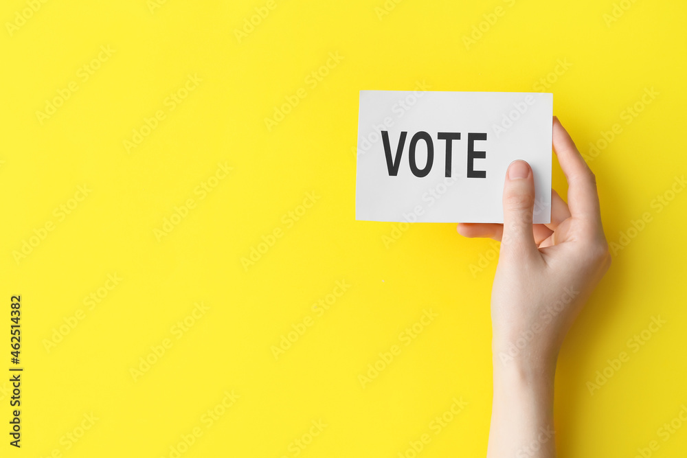 Hand holding paper with text VOTE on color background Hand holding paper with text VOTE on color background