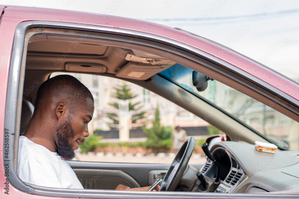 Naklejka premium black man in the front passenger seat of a car using his phone
