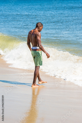 A well built young sexy black guy, half naked, is walking into water of ocean.